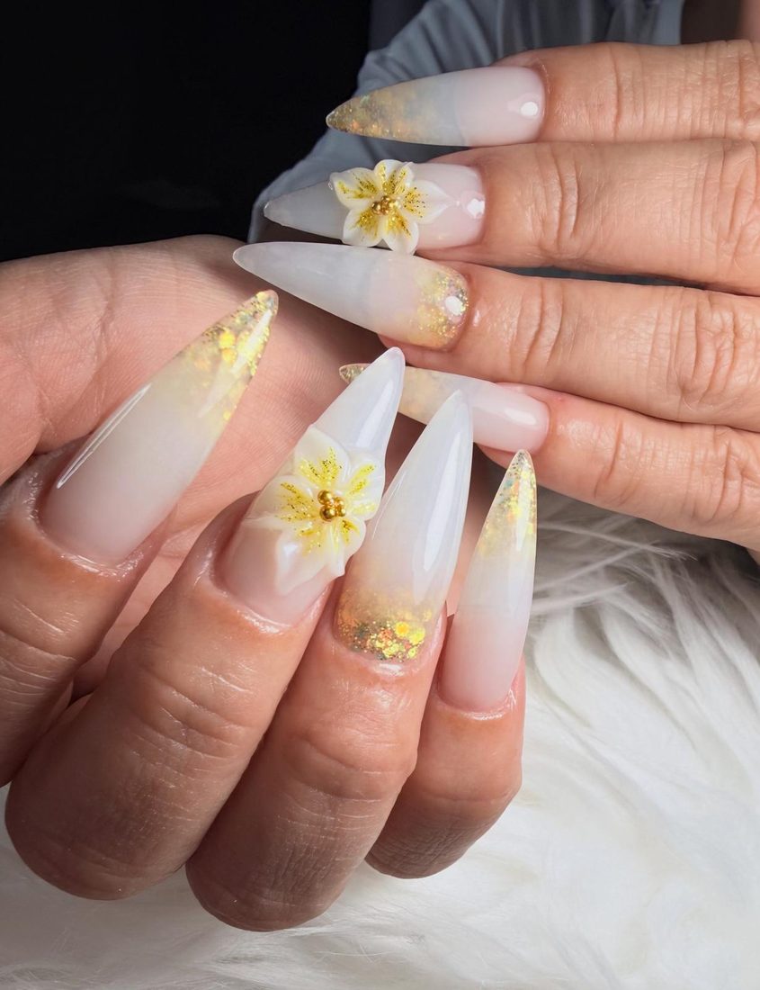 Uñas stiletto nude con glitter dorado y flores 3D